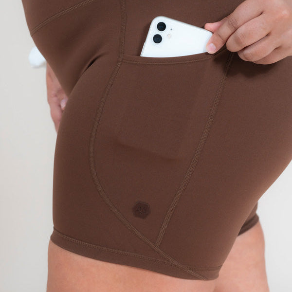 Brown shorts with a pocket holding a white object on a plain background