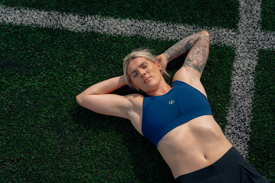 Millie lying on a sports field wearing a blue sports bra and black leggings.
