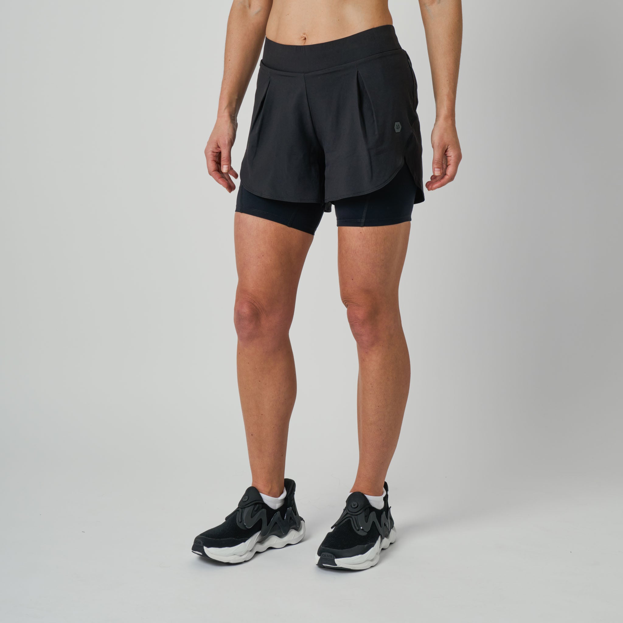 Person wearing black athletic shorts and black sneakers on a gray background