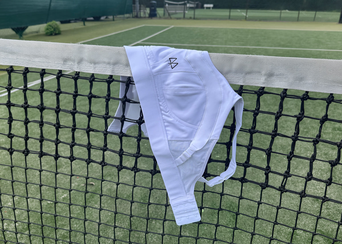 White athletic bra and shorts hanging on a tennis net with a sports field in the background