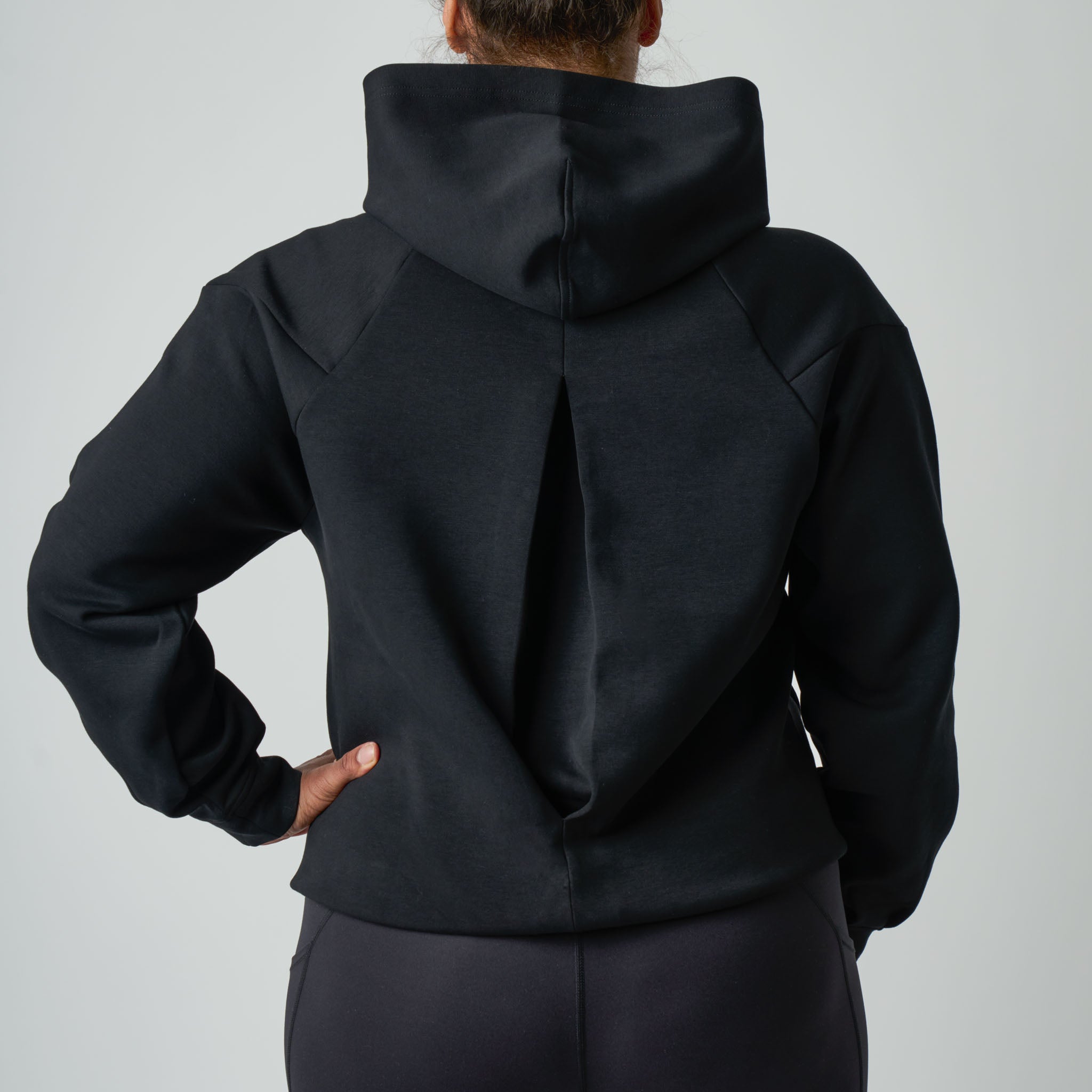 Person wearing a black hoodie from behind on a light gray background