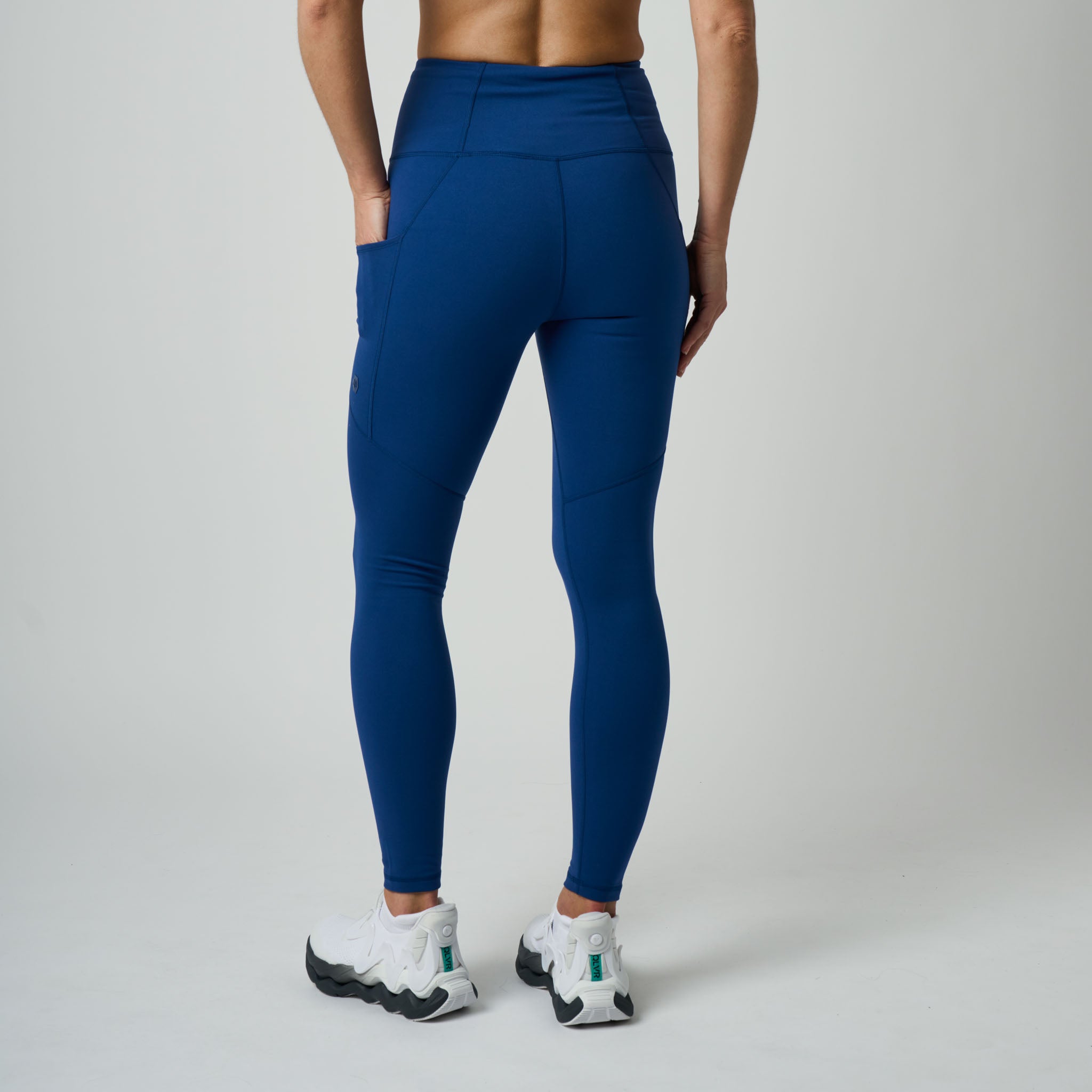 Person wearing blue leggings and white sneakers on a plain background