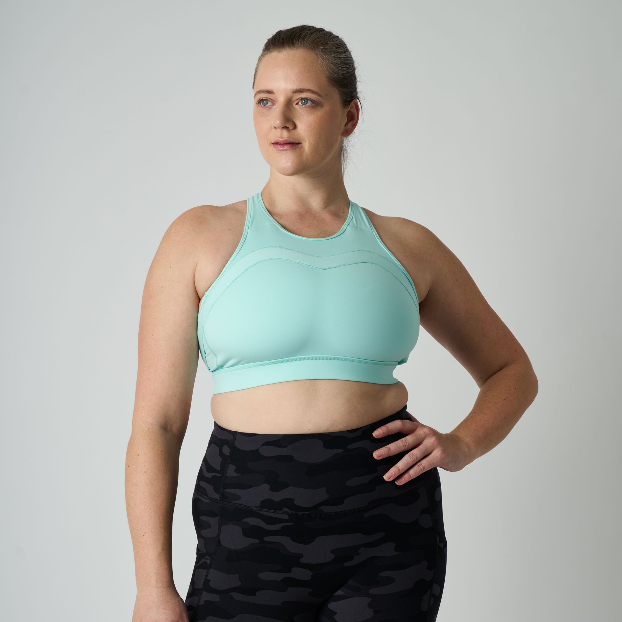 Woman wearing a light blue sports bra and black camouflage leggings on a gray background