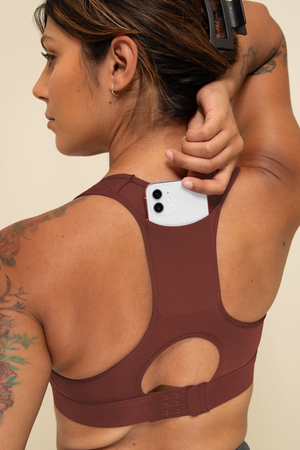 Woman in Burgundy high-support sports bra facing back, showing the phone pocket in the rear of the bra.