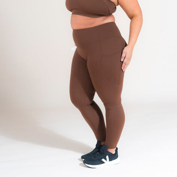 Person wearing brown leggings and navy sneakers on a white background